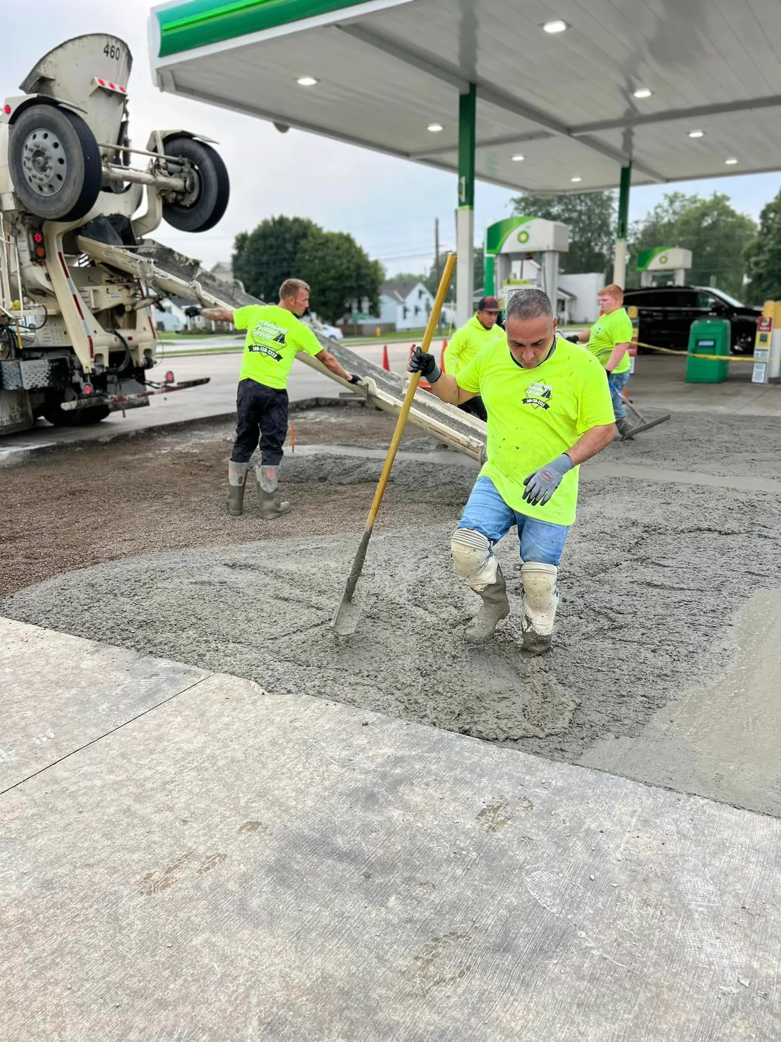 A team of construction workers in neon yellow shirts are pouring and leveling concrete at a gas station.