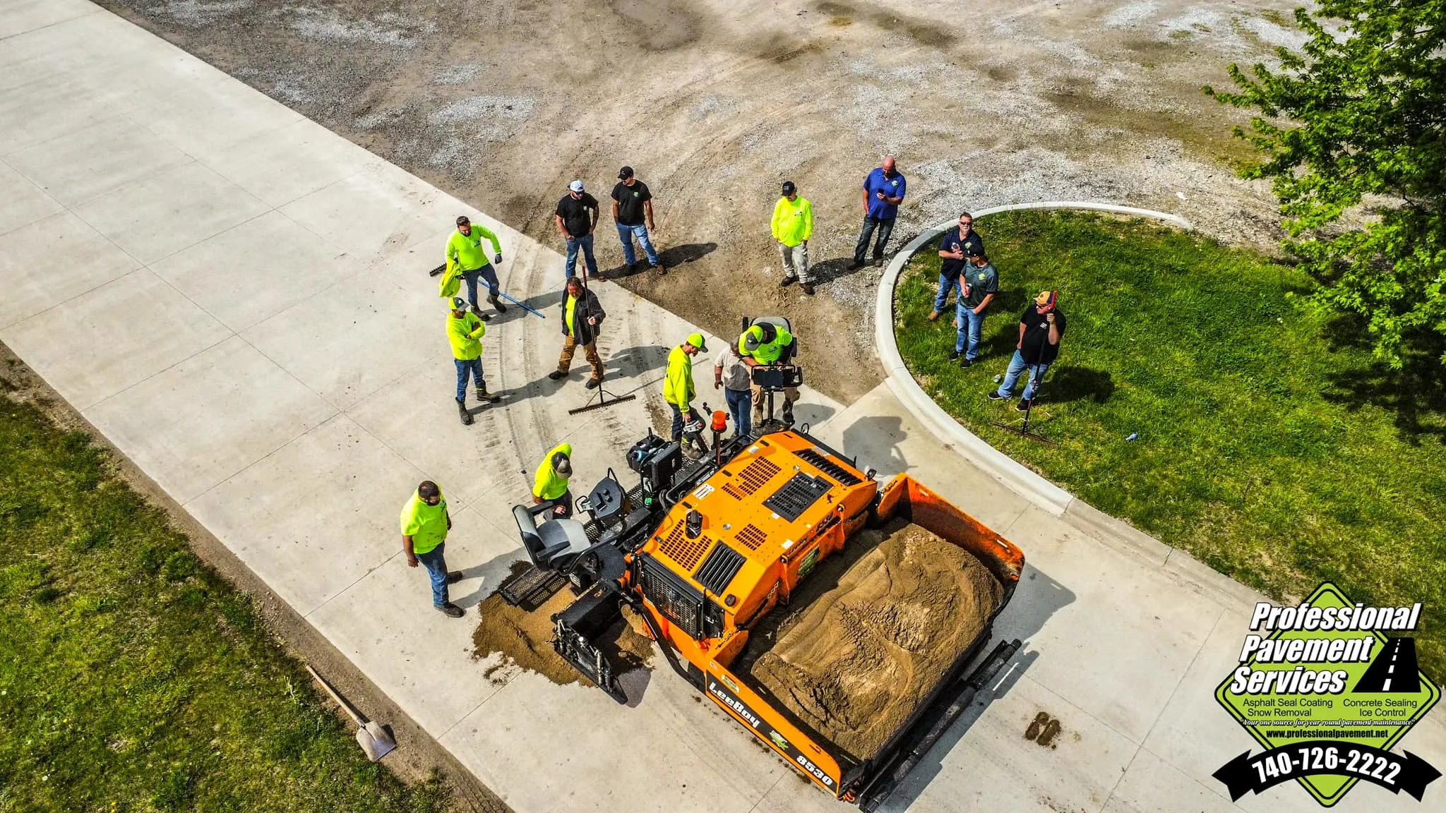An aerial view captures a crew of workers gathered around an orange paving machine, actively engaged in a concrete paving project.