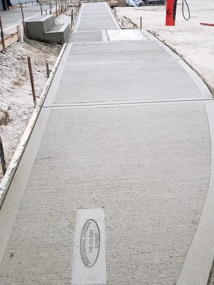 A newly poured concrete sidewalk with various sections and a stamped company logo is shown under construction.
