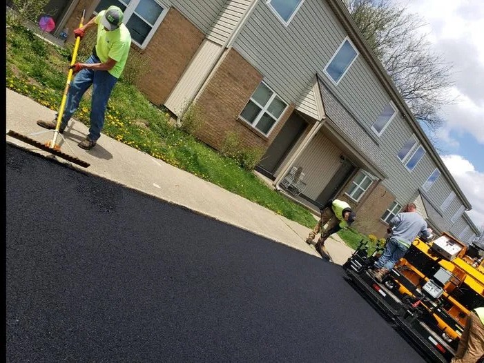 A group of construction workers in neon shirts are pouring and leveling concrete at a gas station, with a concrete truck in the background.          Analysis