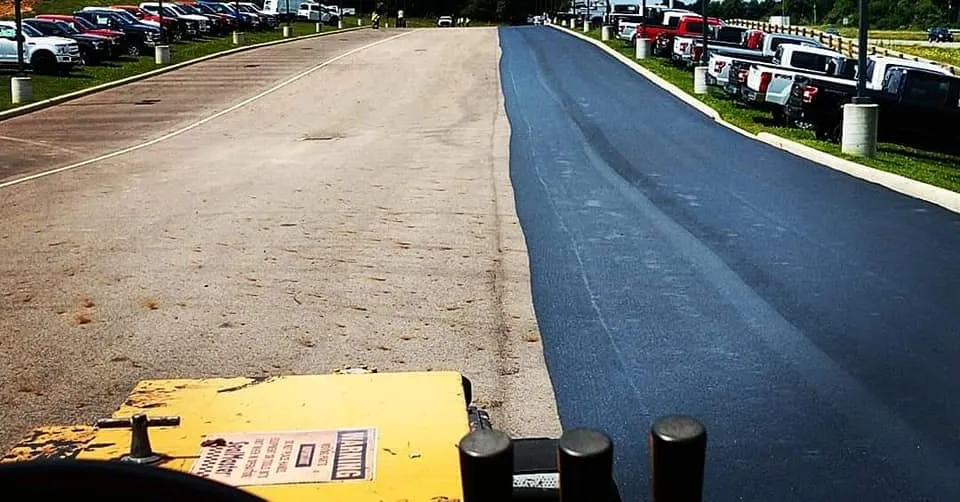 A parking lot shows a stark contrast between newly black sealcoated asphalt and old faded gray asphalt.