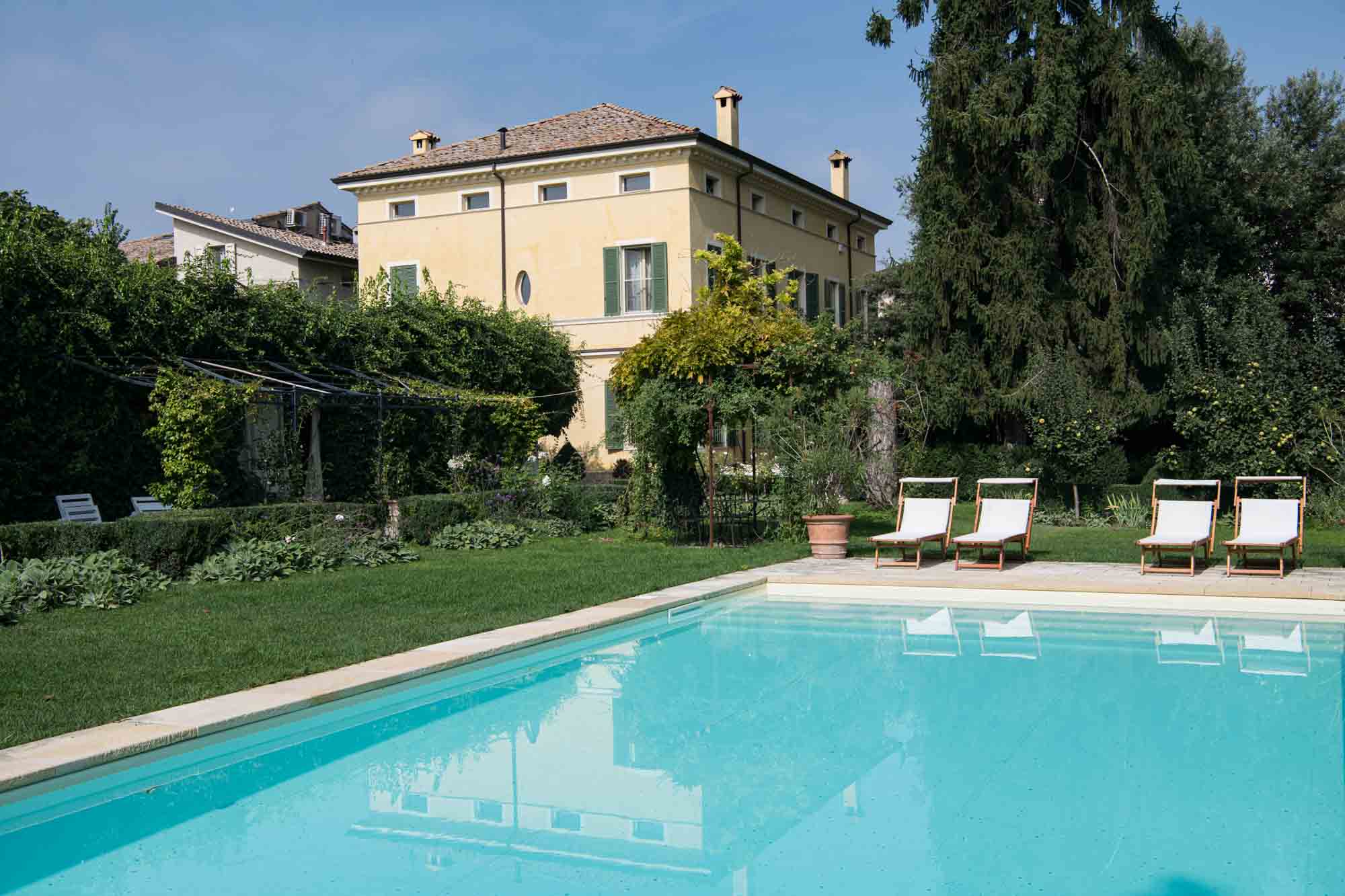 Serene poolside view with sun loungers and a historic Italian villa, surrounded by lush greenery—perfect for relaxing in refined rural elegance.