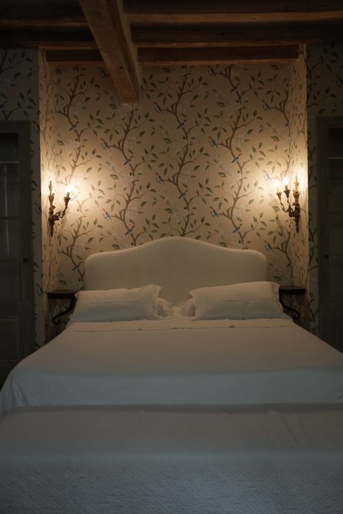 Elegant Italian country-style bedroom with floral wallpaper, antique wall sconces, and rustic wooden beams — exclusive stay in the Italian countryside.