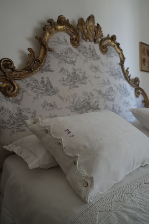 Close-up of an antique French-style upholstered headboard with gilded wood and embroidered pillow — refined country stay in Italy.