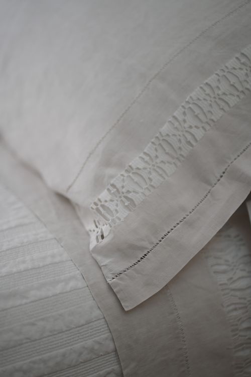 Close-up of soft white linen with lace details — artisanal bedding in an elegant countryside retreat.