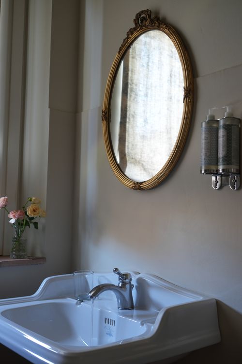 Detail of classic ceramic sink and antique mirror with floral decor — romantic bathroom in a countryside guesthouse.