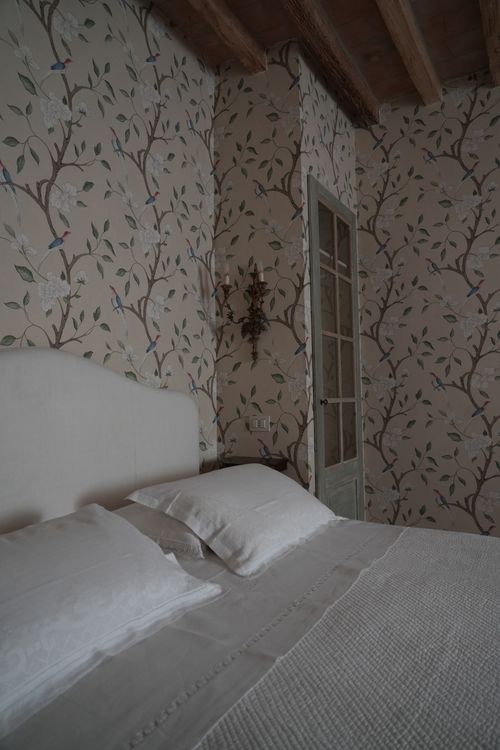 Close-up of a white linen bed in a refined country-chic room with nature-inspired wallpaper — boutique accommodation in rural Italy.