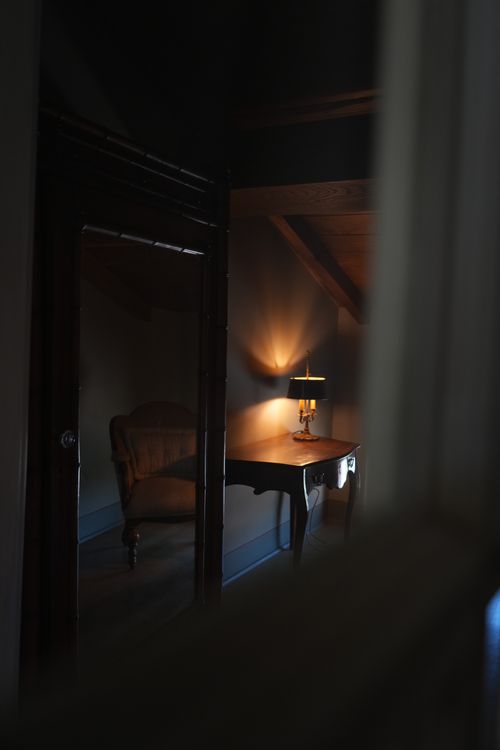 Warm-lit writing desk and vintage armchair reflected in a mirror — cozy retreat with timeless Italian charm.