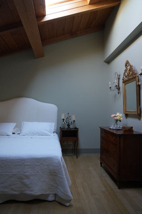 Elegant bedroom with skylight, antique furniture and white linen bed — serene country house ambiance.