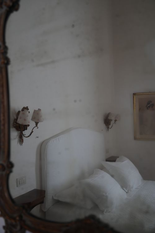 Soft white bed reflected in an antique mirror — romantic rustic interior with vintage charm.