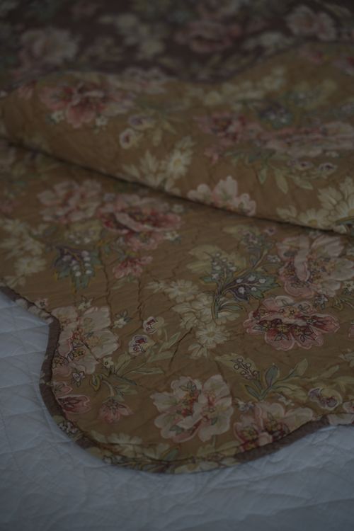 Close-up of vintage floral quilt in soft earthy tones — timeless Italian bedroom textile.