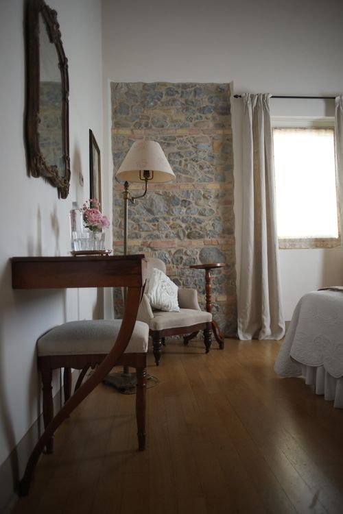 Corner of a rustic-chic bedroom with exposed stone wall, floor lamp, vintage mirror and fresh flowers.