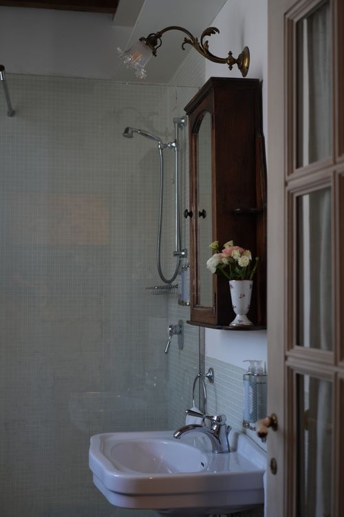 Authentic countryside bathroom with antique wood cabinet, fresh flowers, and mosaic tiles—perfect for an immersive Italian home experience.