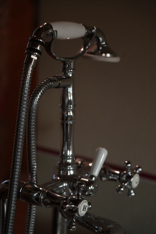 Detail of an artisanal chrome bathtub faucet with porcelain accents, ideal for lovers of antiques and handcrafted design in Italy.
