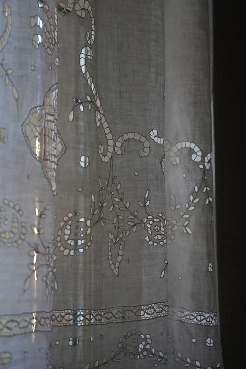 Hand-embroidered linen curtain filtering soft light in a rustic Italian bathroom—celebrating local craftsmanship and timeless charm.