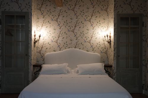 Charming country-style bedroom with antique wall sconces, floral wallpaper, and a soft linen headboard – perfect for an exclusive Italian stay surrounded by timeless elegance.