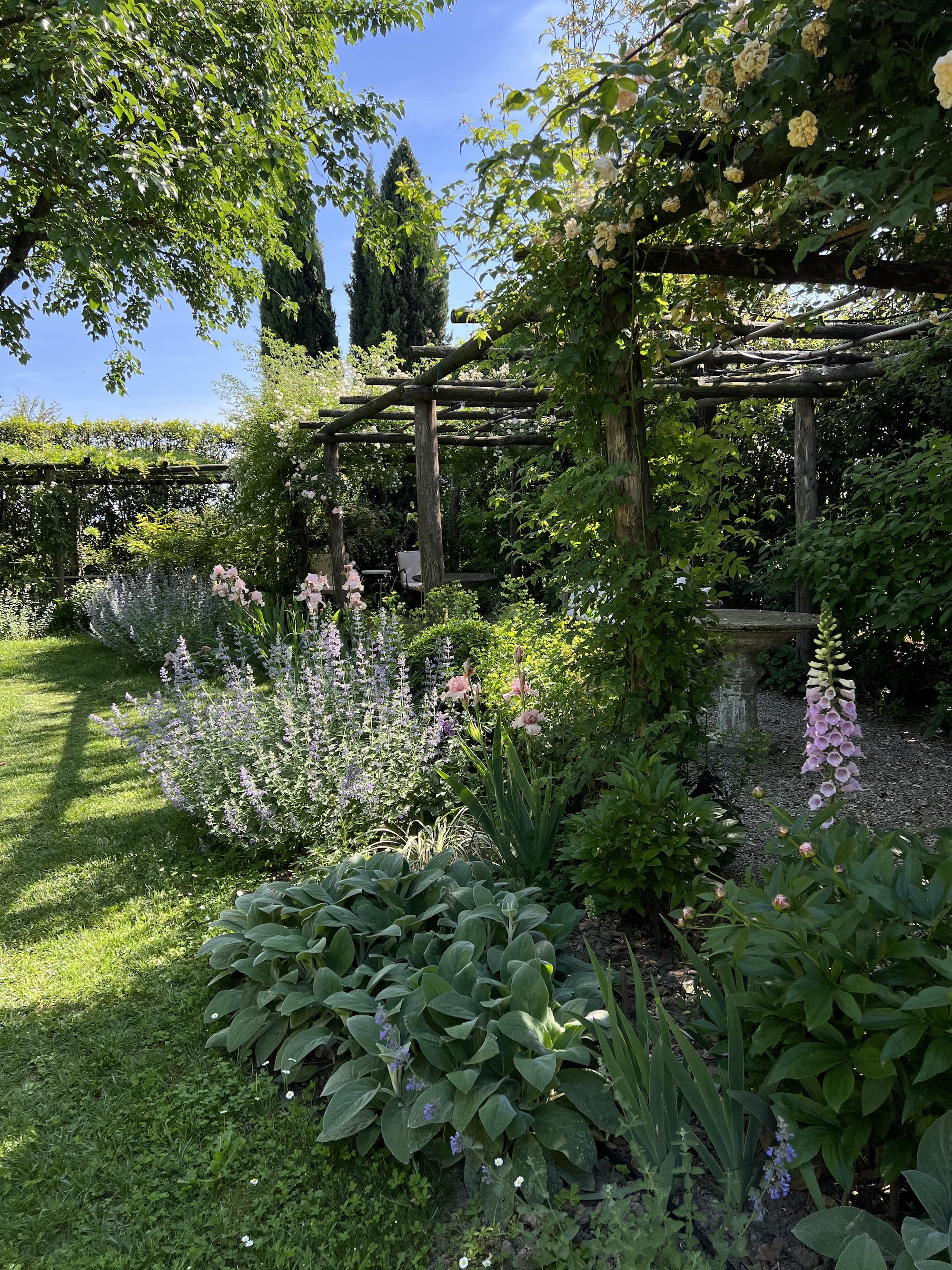 Charming Italian garden with a wooden pergola and lush flower beds, ideal for nature lovers seeking a peaceful retreat.