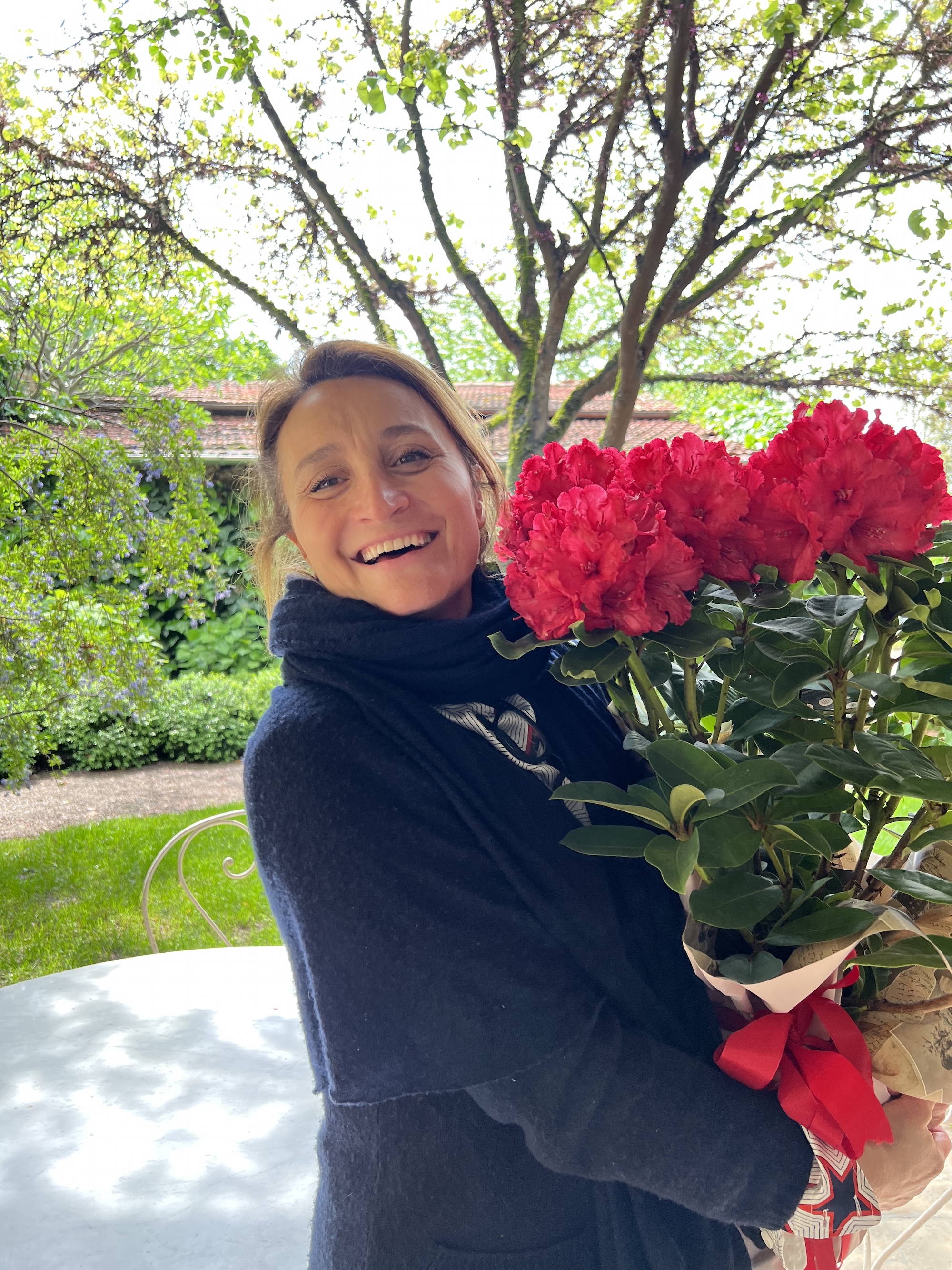 Person in patterned shirt arranging a bouquet of pink and red roses with green leaves in a glass vase.