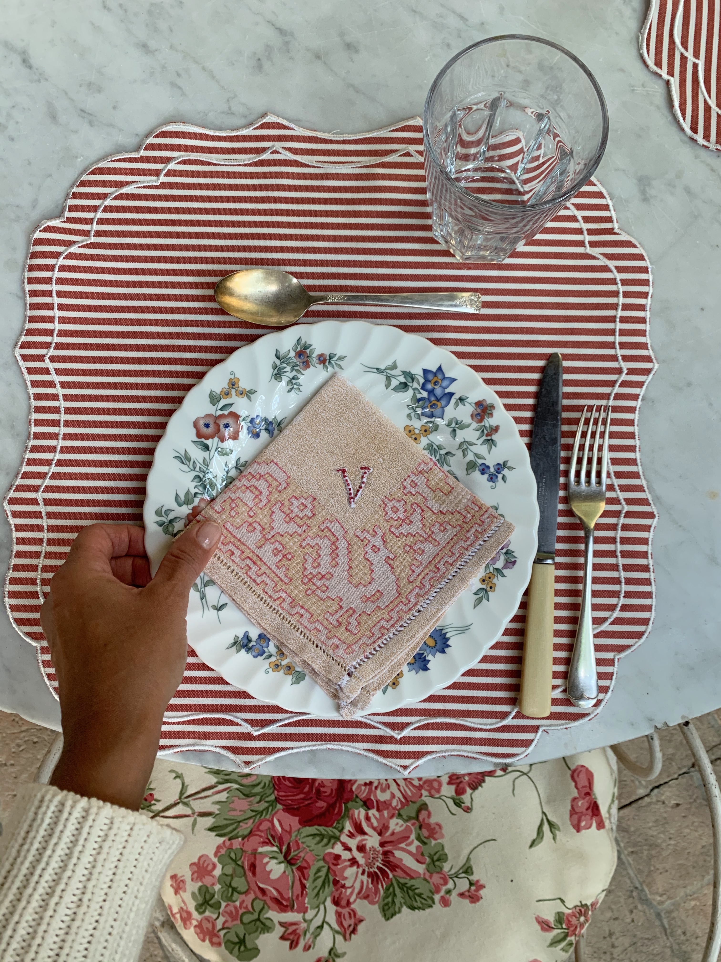 Outdoor romantic table with floral plates and striped placemats, ready for an Italian countryside meal.