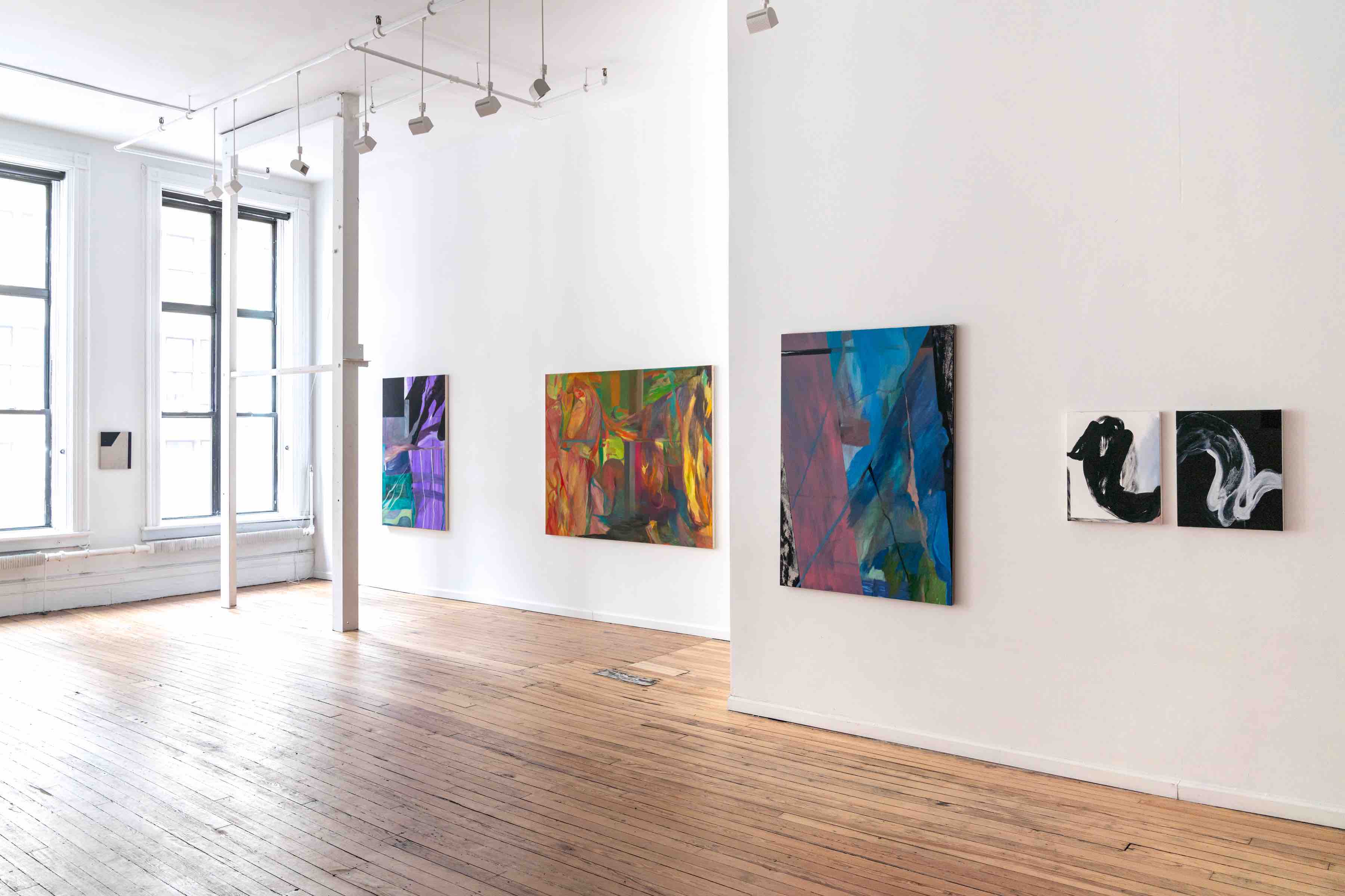 Bright art gallery with wooden floors and five abstract paintings displayed on white walls.