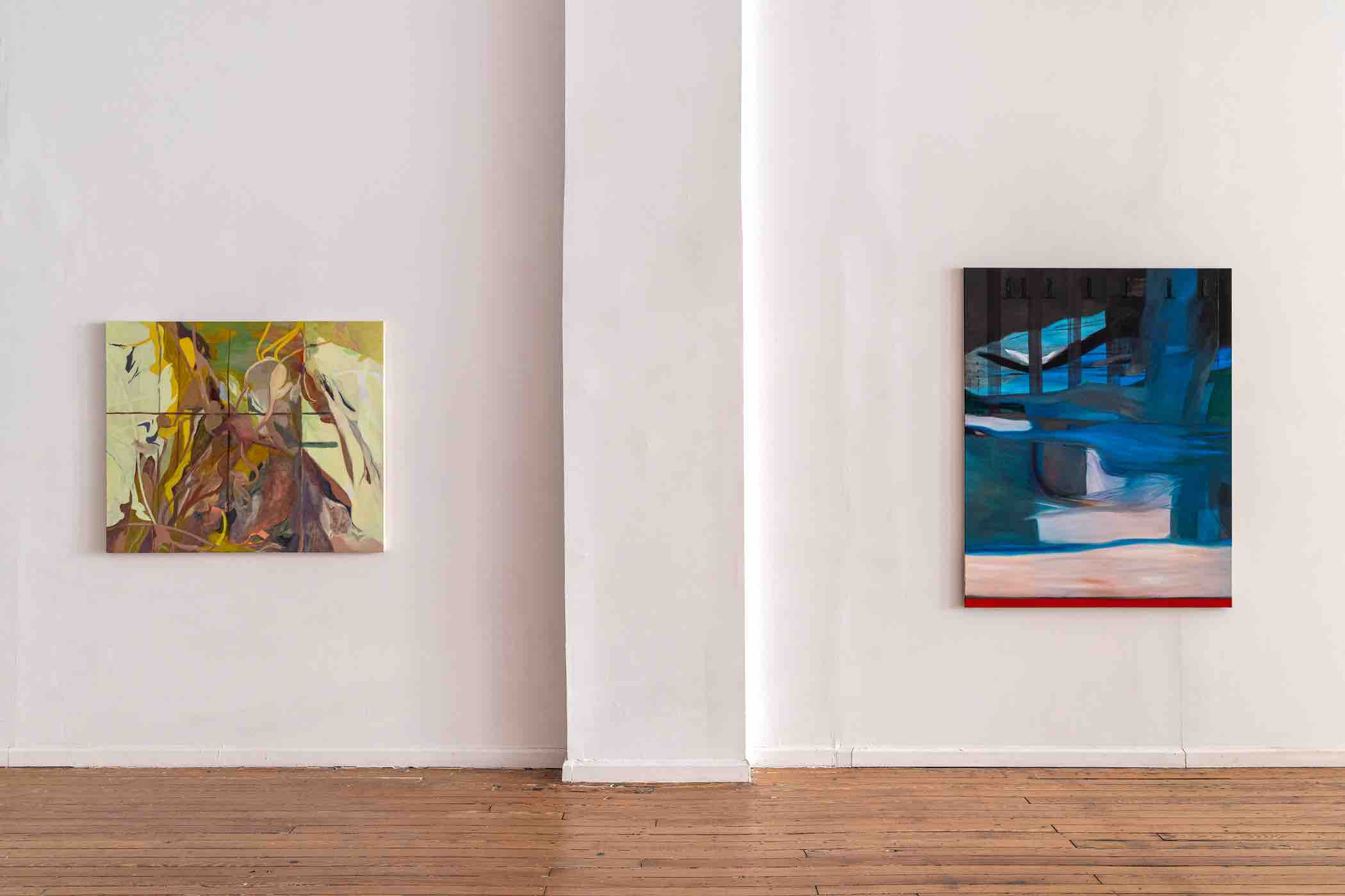 Two abstract paintings hanging on a white wall with wooden floor; the left painting features earth tones and organic shapes, the right painting contains blue, black, and red abstract forms.