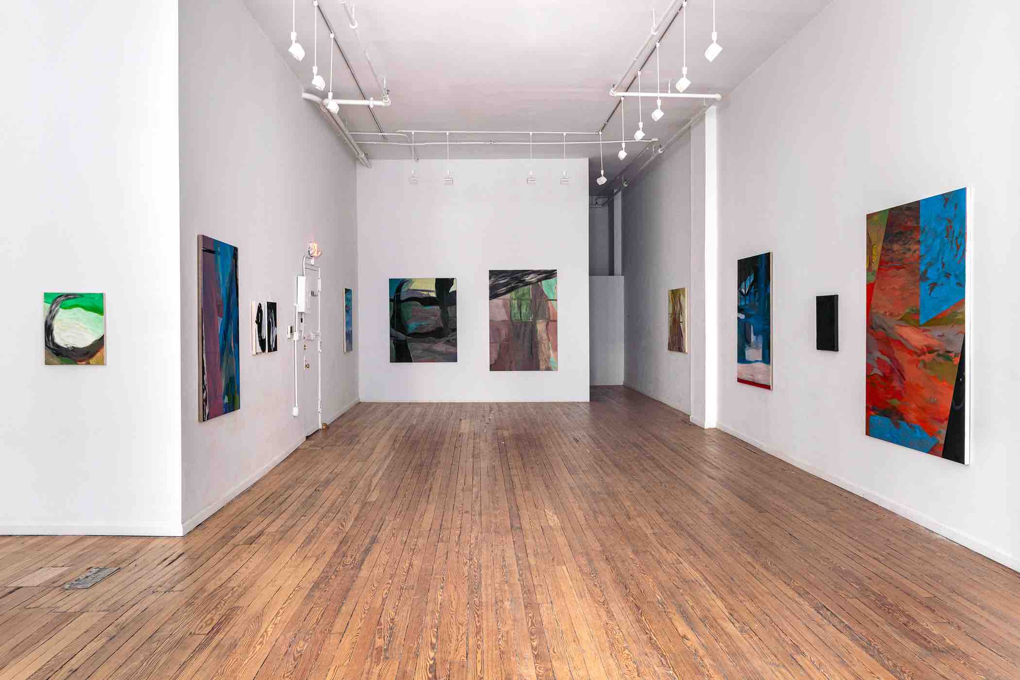 Wide art gallery with wooden floors and white walls featuring abstract colorful paintings.