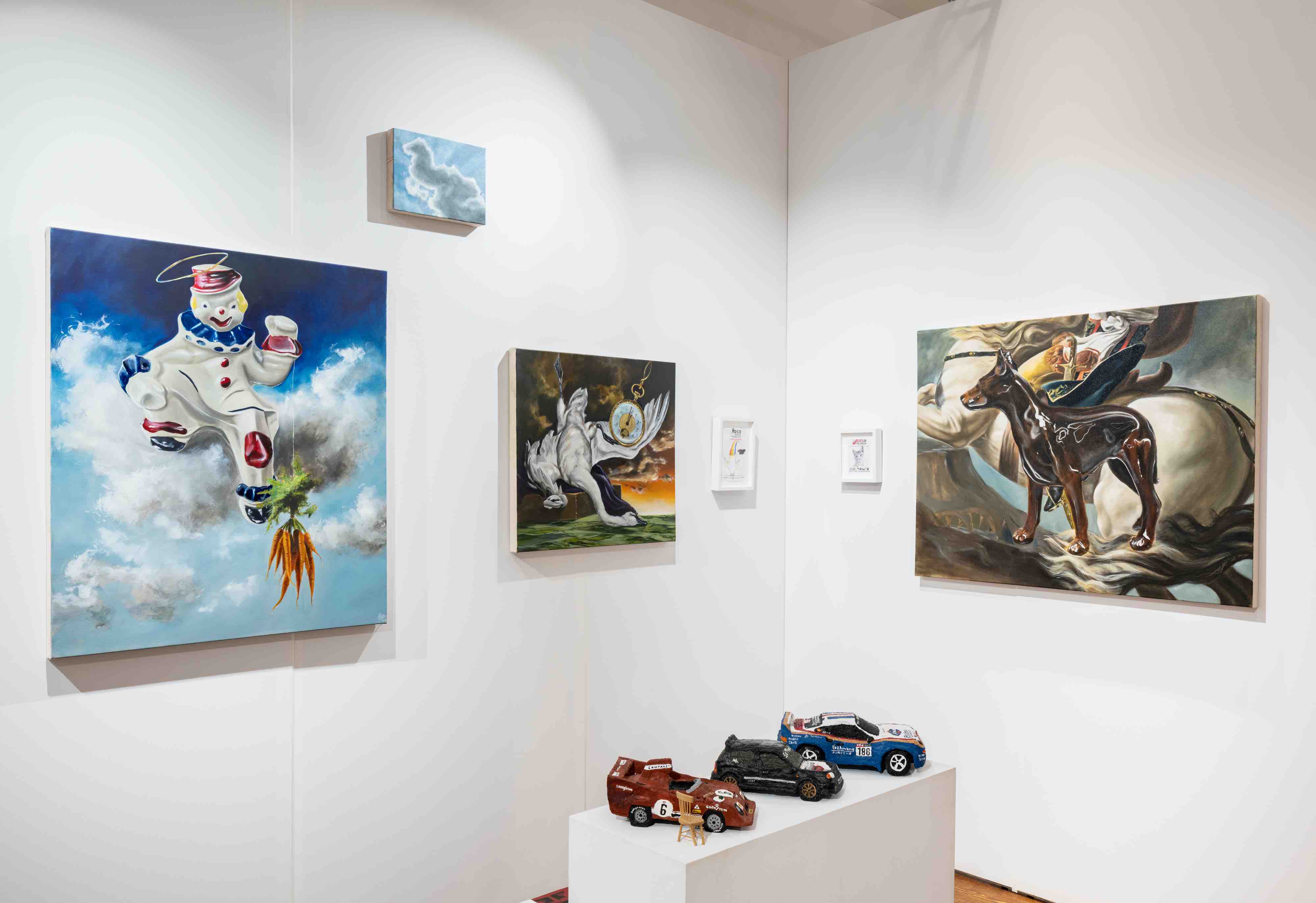 Gallery corner with paintings featuring a playful clown figure, a horse with a dog, and a winged figure with a clock, alongside three toy cars on a white pedestal.
