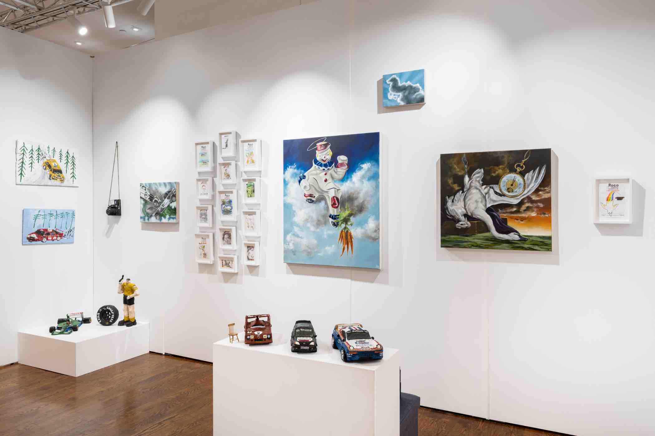 Gallery room with various artworks including paintings of cars, a snowman on a cloud holding a carrot, a figure with a pocket watch, framed sketches, and model cars displayed on white pedestals.