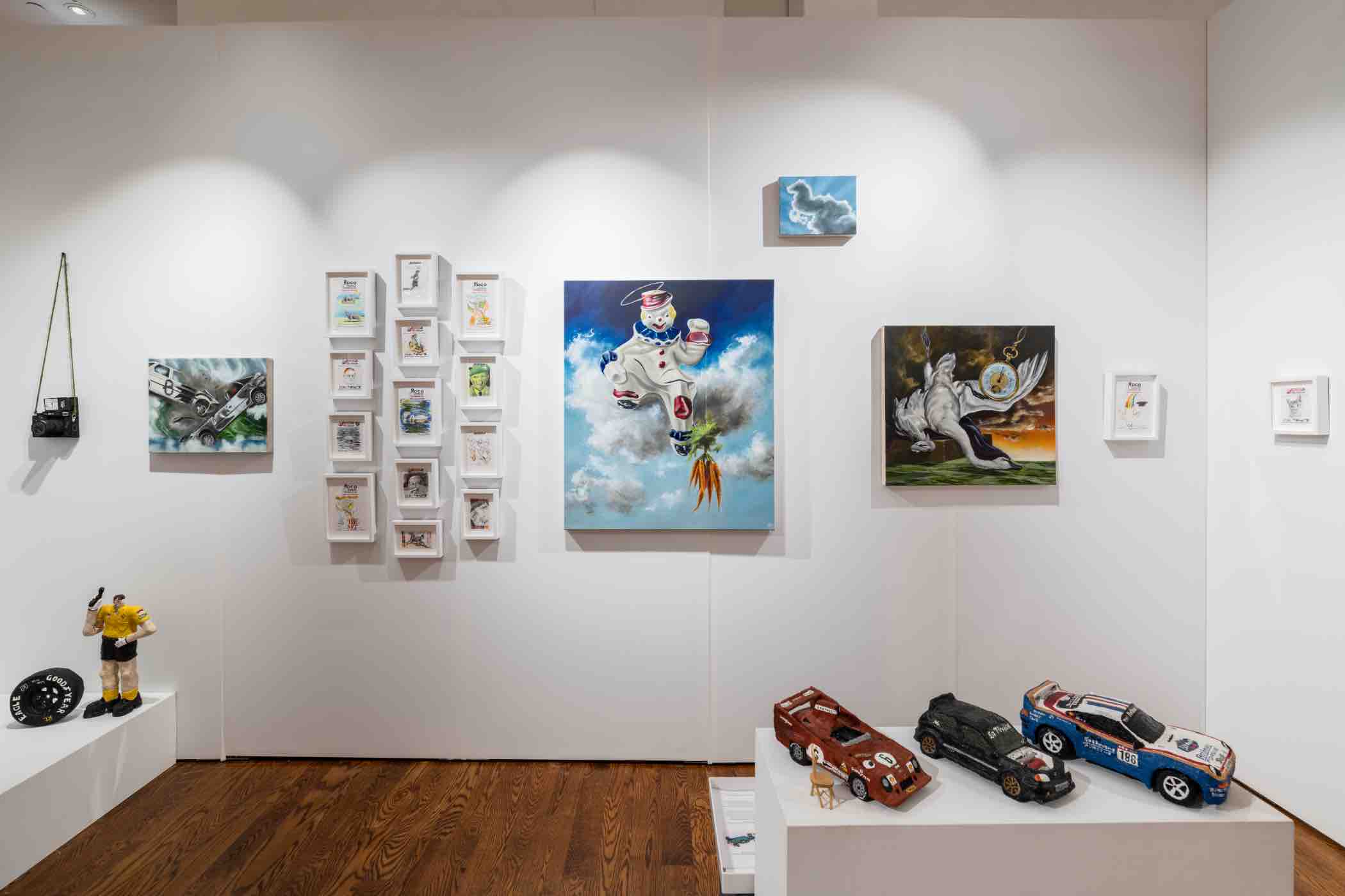 Gallery wall with various artworks including a painted astronaut, a horse with wings, multiple small framed illustrations, toy race cars on pedestals, and a hanging vintage camera.