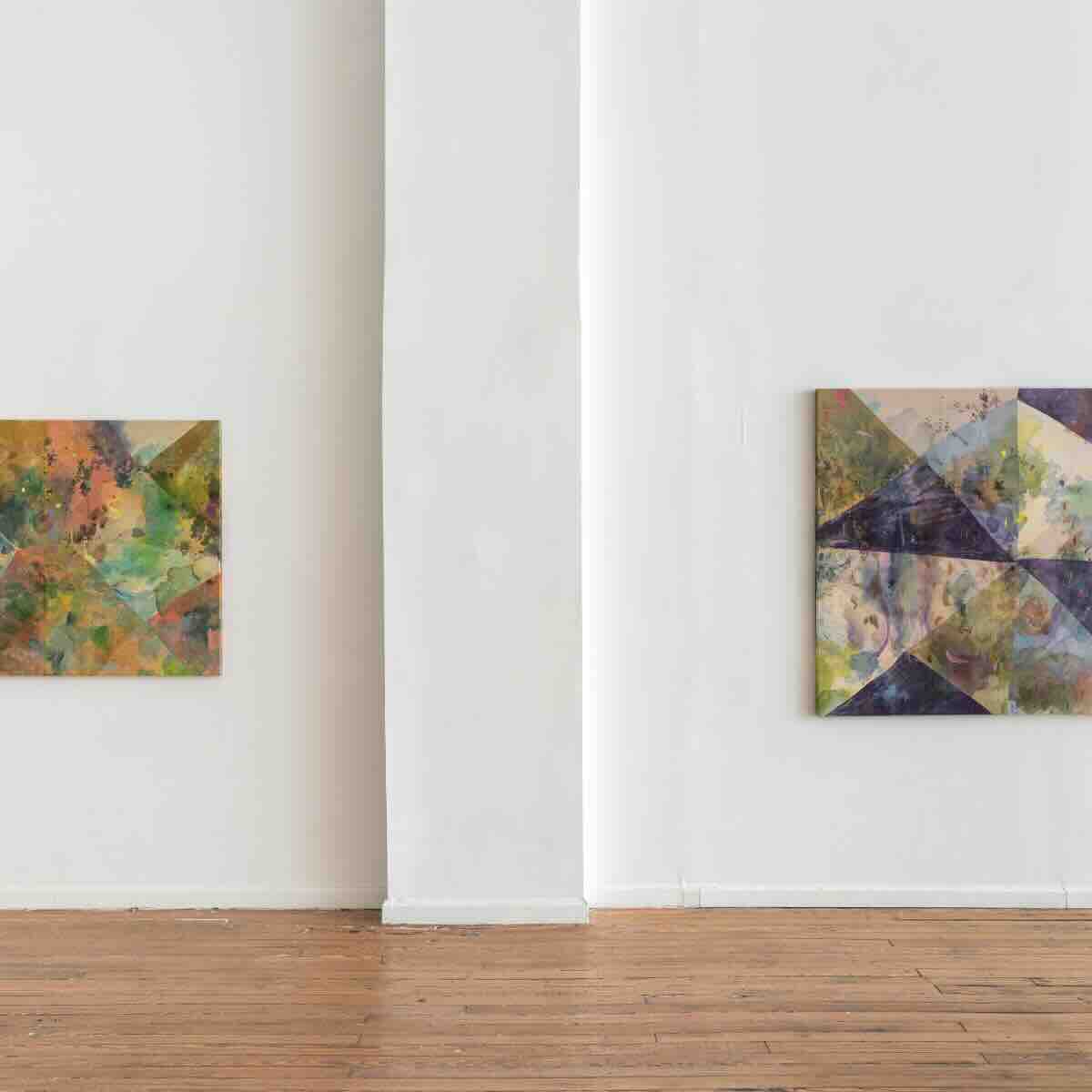 Two abstract geometric paintings with multicolored shapes hanging on white walls in a minimal gallery space with wooden floor.