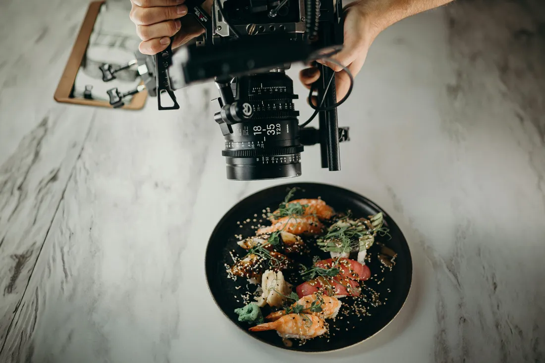 Close-up of a camera filming a sushi plate on a white marble surface.