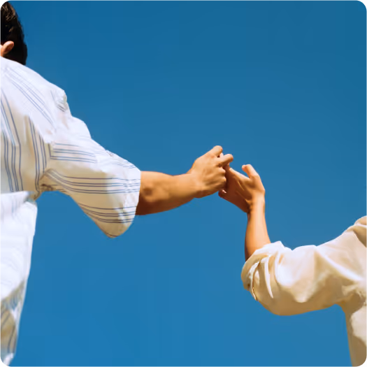Two people reaching out and gently holding each other's pinky fingers against a clear blue sky.