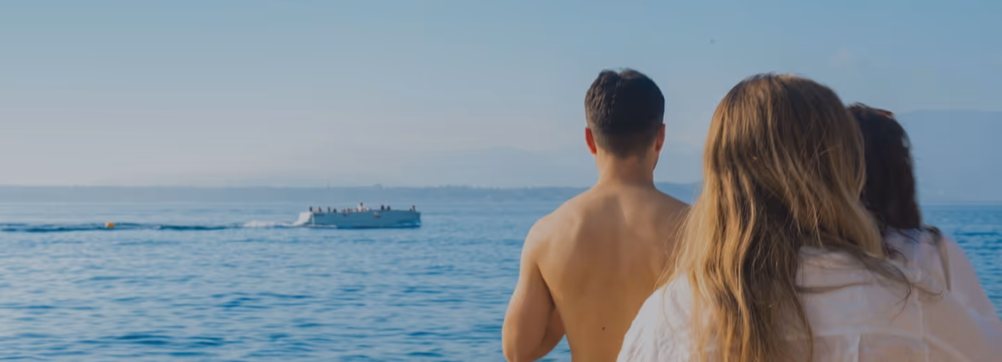 Three people looking out over a calm sea with a boat in the distance on a clear day.