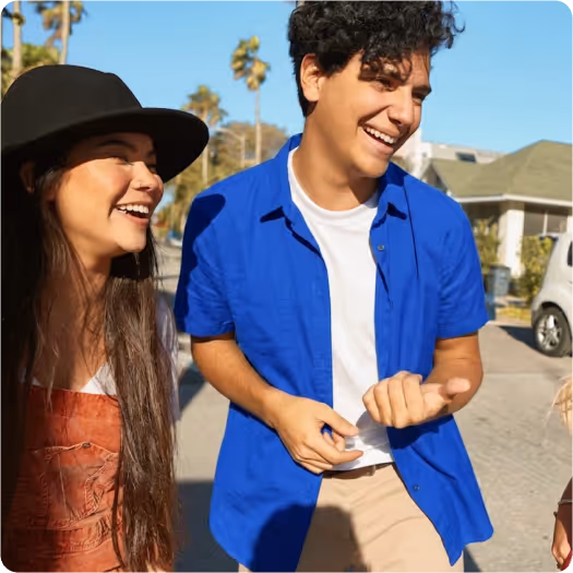 Smiling young man in a blue shirt and young woman wearing a black hat walking outdoors on a sunny day.