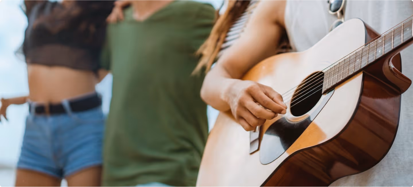 Close-up of a person playing an acoustic guitar with two others standing closely in the background.