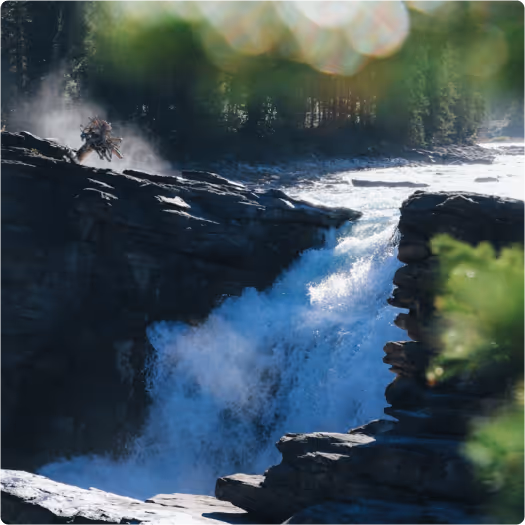 Waterfall flowing powerfully over rocky cliffs surrounded by forest and mist.