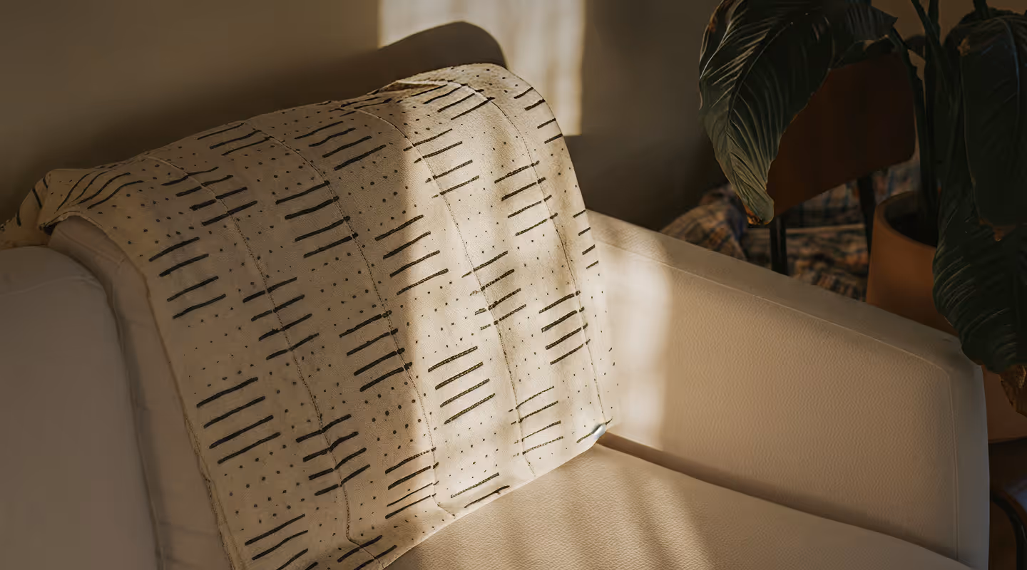 Soft beige sofa with a patterned light-colored throw blanket draped over the armrest, next to a large green potted plant.