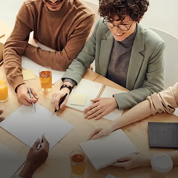 Four people collaborating at a table with notebooks, papers, and drinks.