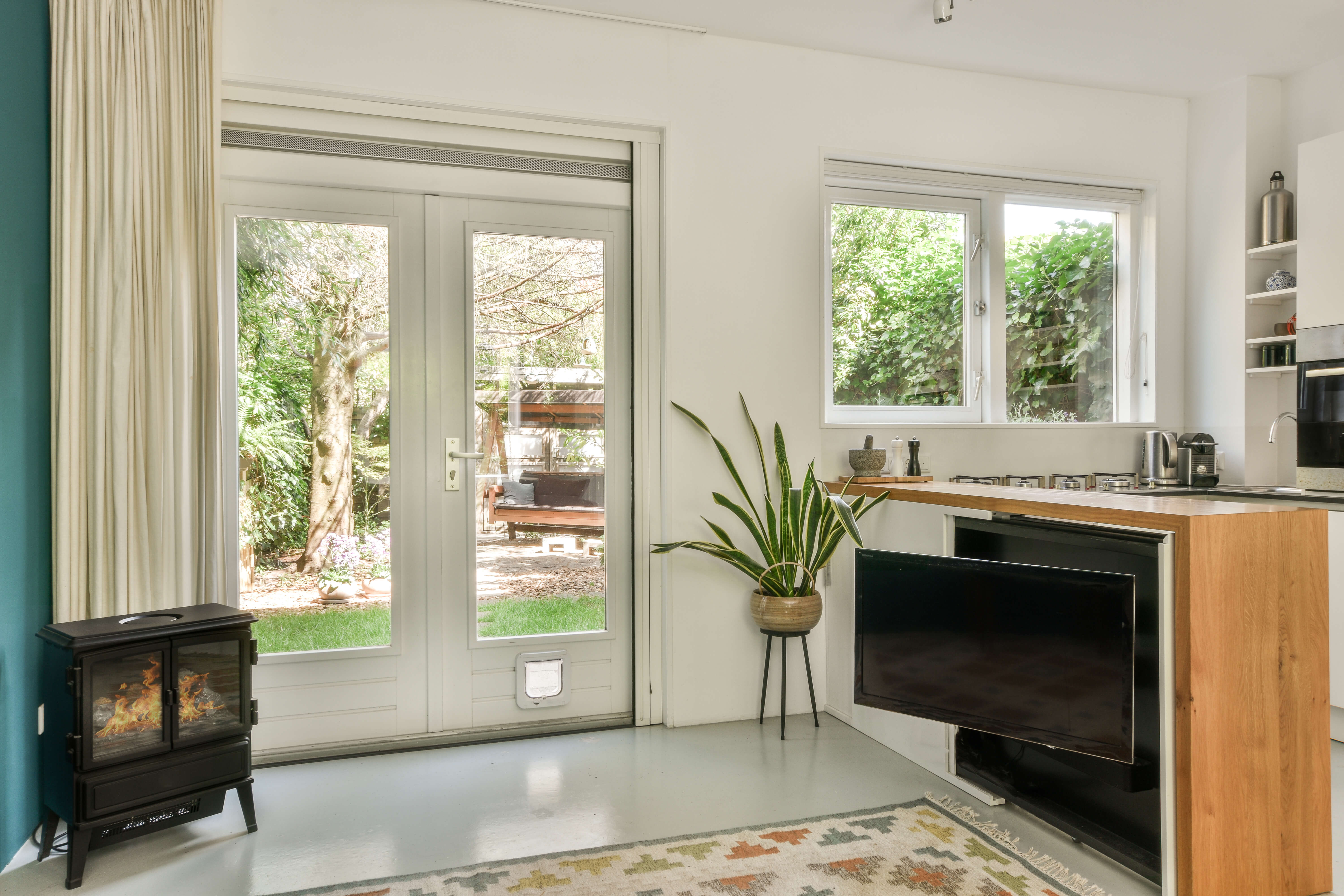 Bright ADU interior with glass doors, large windows, compact kitchen, and a cozy view of a landscaped backyard in Denver.