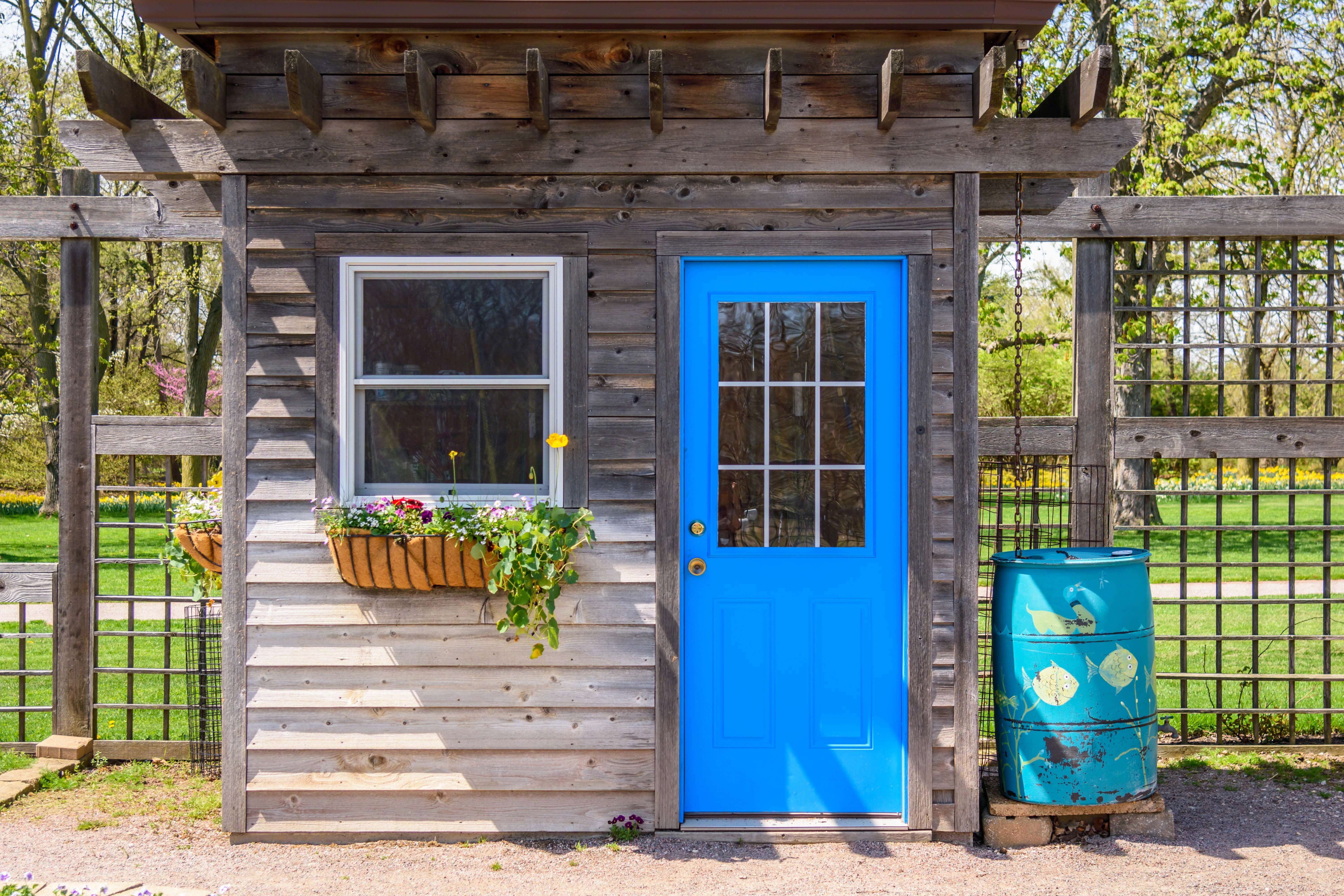 Rustic Denver backyard ADU with weathered wood siding, bright blue door, flower boxes, and outdoor rain barrel.