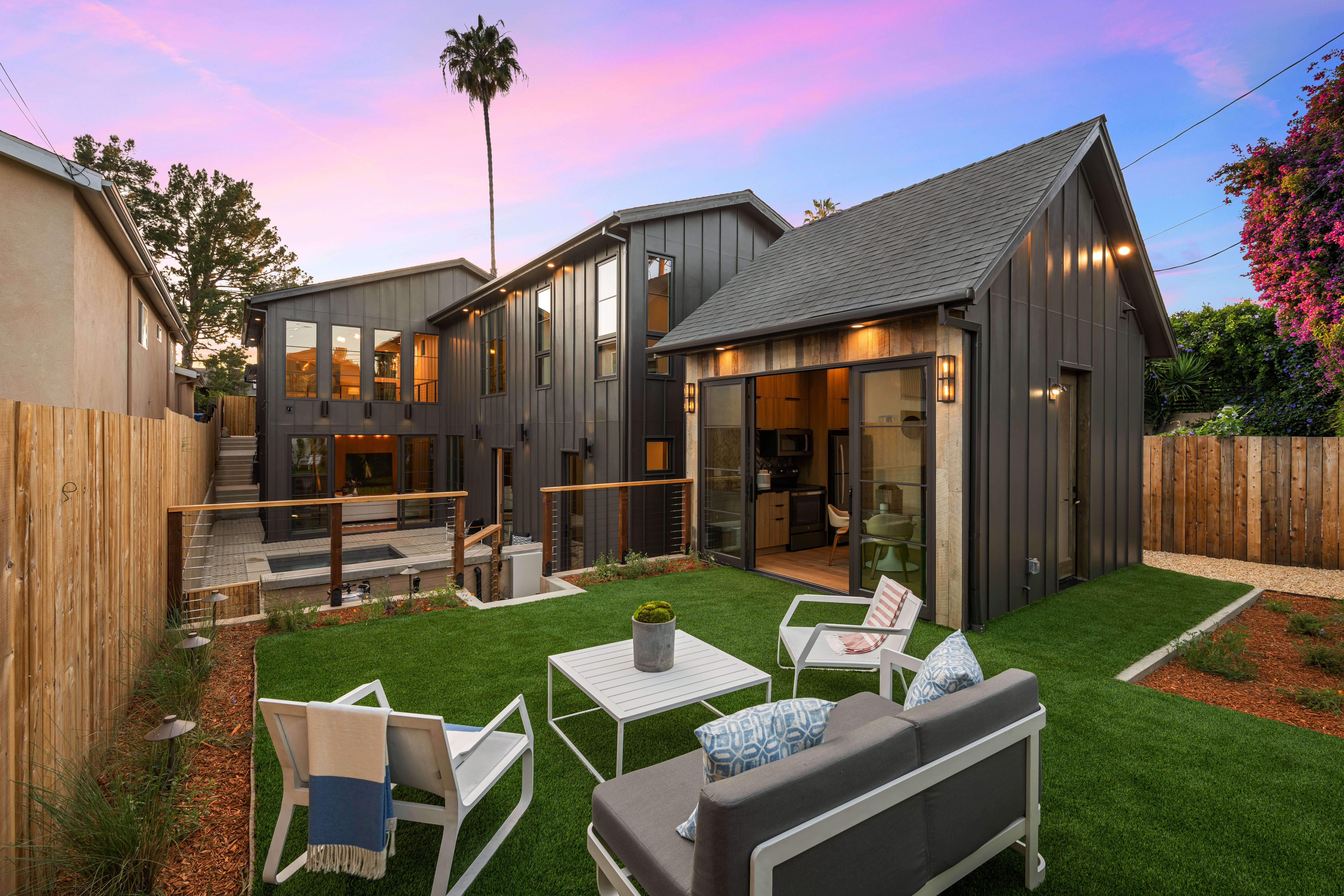 Contemporary detached ADU with a sleek black exterior, large sliding glass doors, and wood steps leading to a landscaped yard.