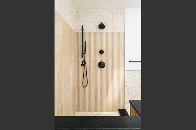 Modern shower remodel with vertical tile detail, matte black fixtures, and natural stone flooring.