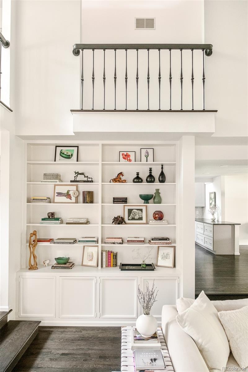 Built-in white shelving filled with books and decor in a remodeled Hilltop Denver home, with a view toward the kitchen.