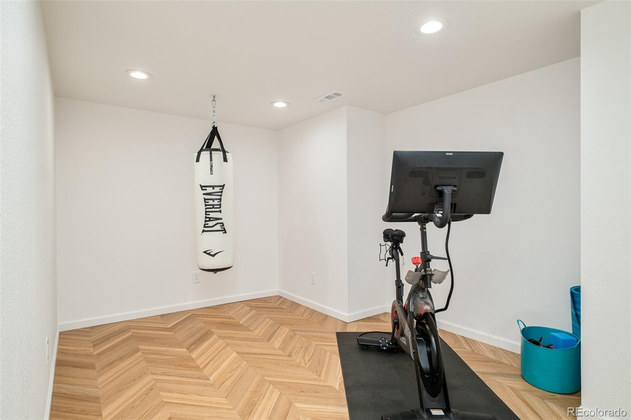 Home gym space in a remodeled Hilltop Denver home featuring herringbone wood floors, a Peloton bike, and punching bag.
