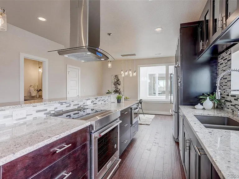 Kitchen island and cooktop view with dramatic vent hood and marble backsplash