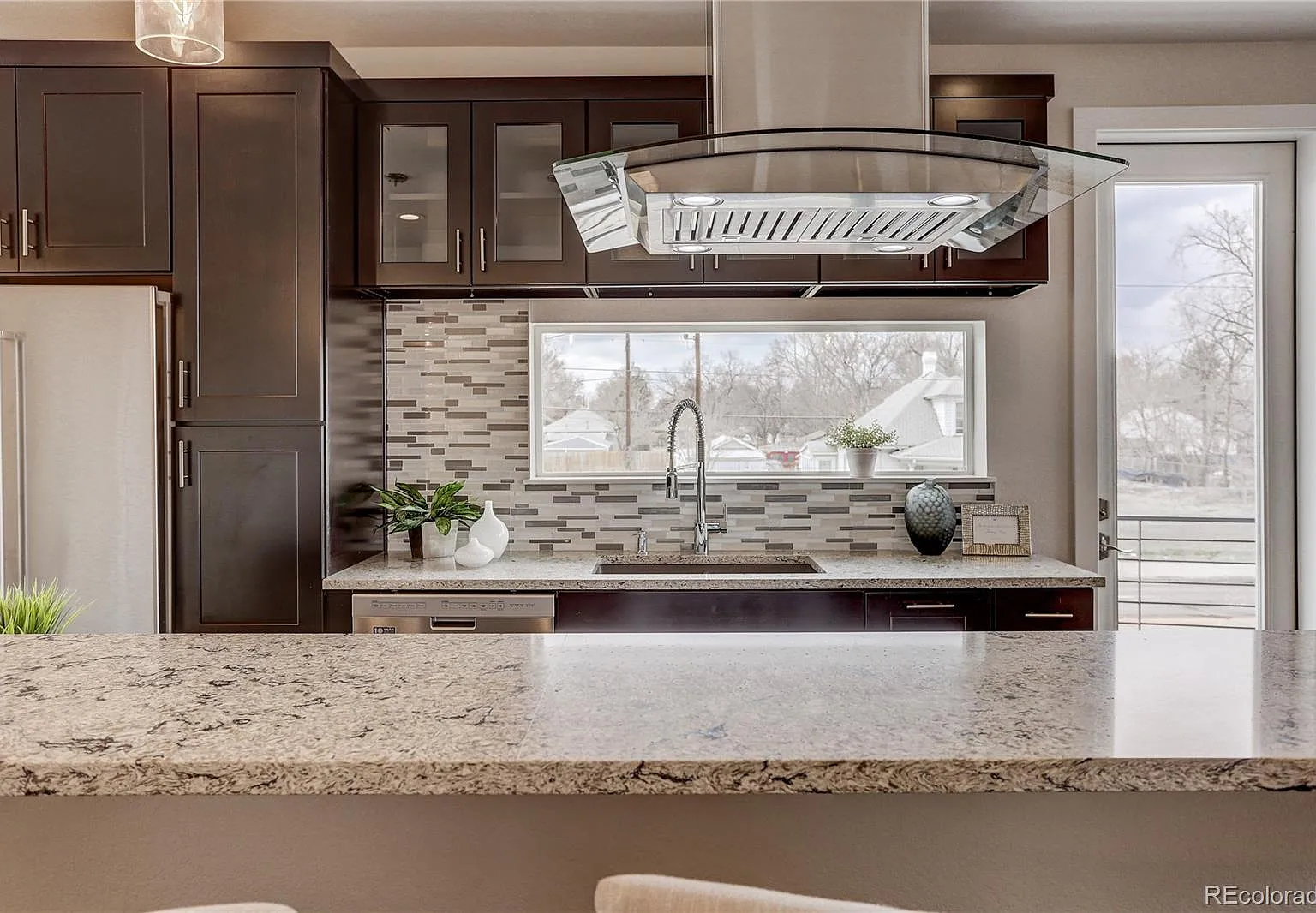 View from the dining room into a sleek kitchen with mirrored backsplash and custom range hood