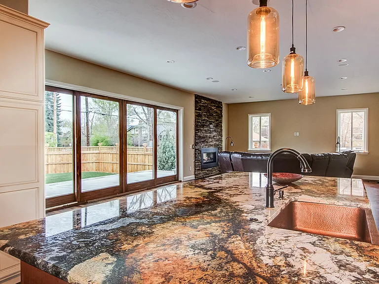 Open-concept living area with sliding glass doors, rustic beam ceiling, and natural stone counters