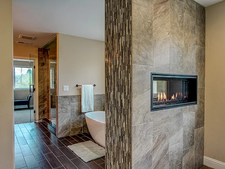 Modern ensuite bathroom featuring a freestanding tub, walk-in shower, and double-sided fireplace