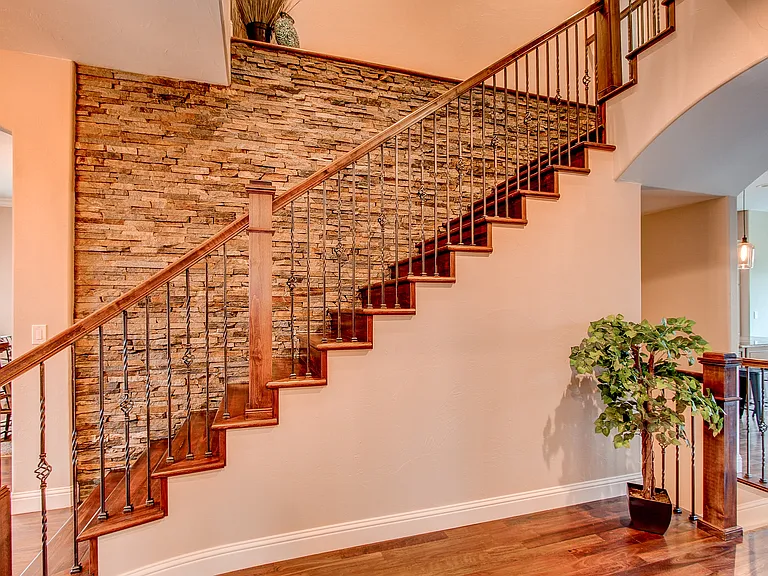 Statement staircase with wood railings and stone accent wall creating a grand entry focal point