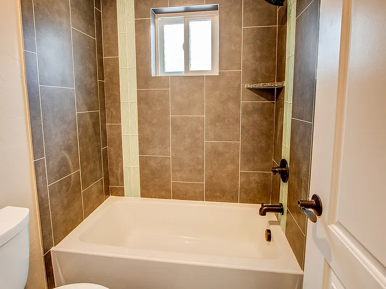 Compact bathtub and shower with large rectangular tiles and dark fixtures in a modern style